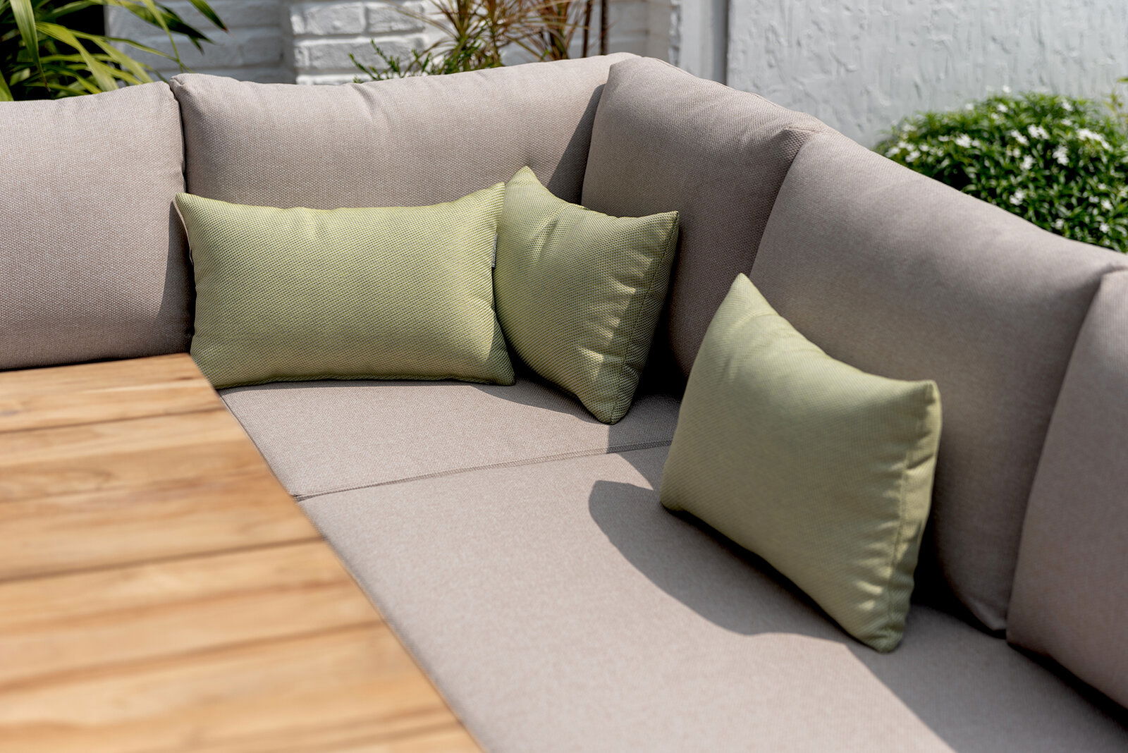 Eck-Sitzbank mit beigen Polstern und grünen Kissen, im Freien neben einem Holztisch, seitliche Perspektive