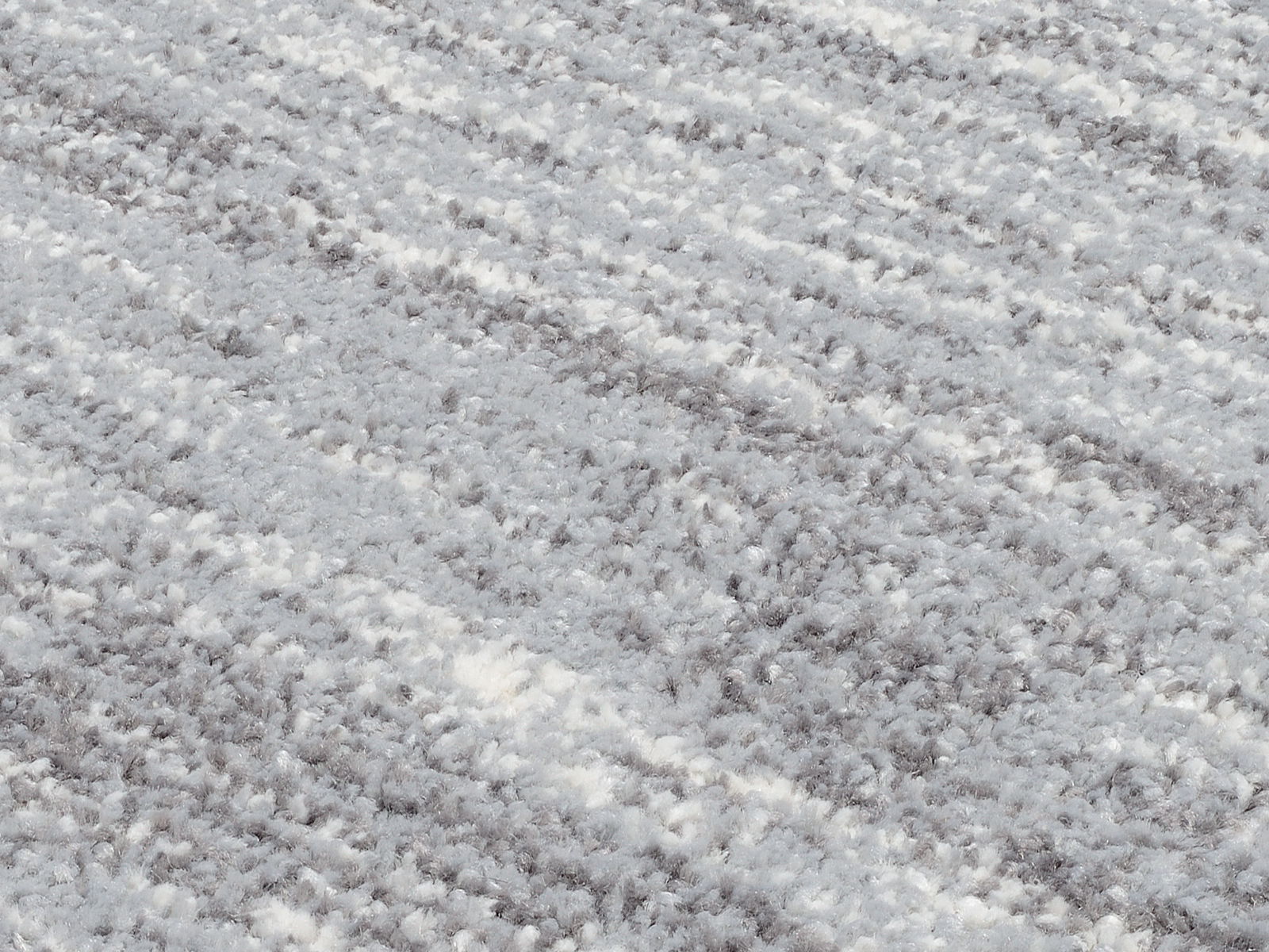 Nahaufnahme eines Uni-Teppichs mit weicher, flauschiger Textur in Grau- und Weißtönen, schräg von oben fotografiert.