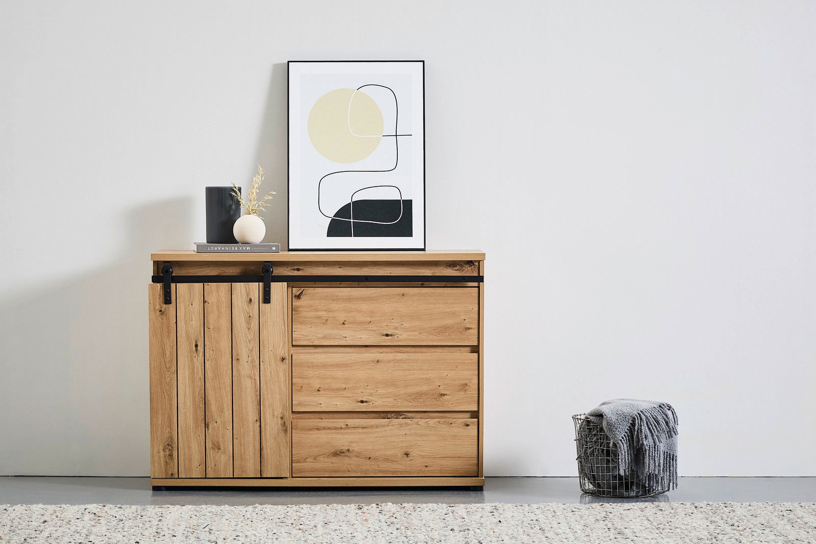 Holzkommode mit Schiebetür und drei Schubladen, dekoriert mit einem gerahmten Bild und Vasen, aus frontaler Perspektive.