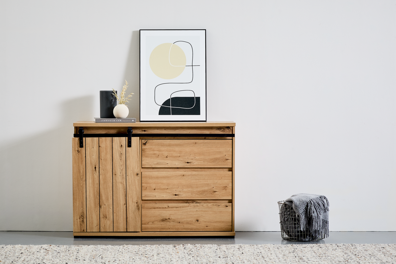 Holzkommode mit Schiebetür und drei Schubladen, dekoriert mit einem gerahmten Bild und Vasen, aus frontaler Perspektive.