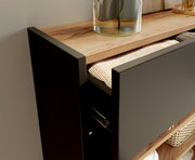 Nahaufnahme eines Hängeschuhschranks mit geöffneter Schublade, die einen geflochtenen Korb zeigt. Die Oberfläche ist aus Holz und darauf steht eine Glasvase. Perspektive von der Seite.