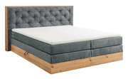 Boxspringbett mit grauem Stoffbezug und Holzrahmen, seitliche Perspektive