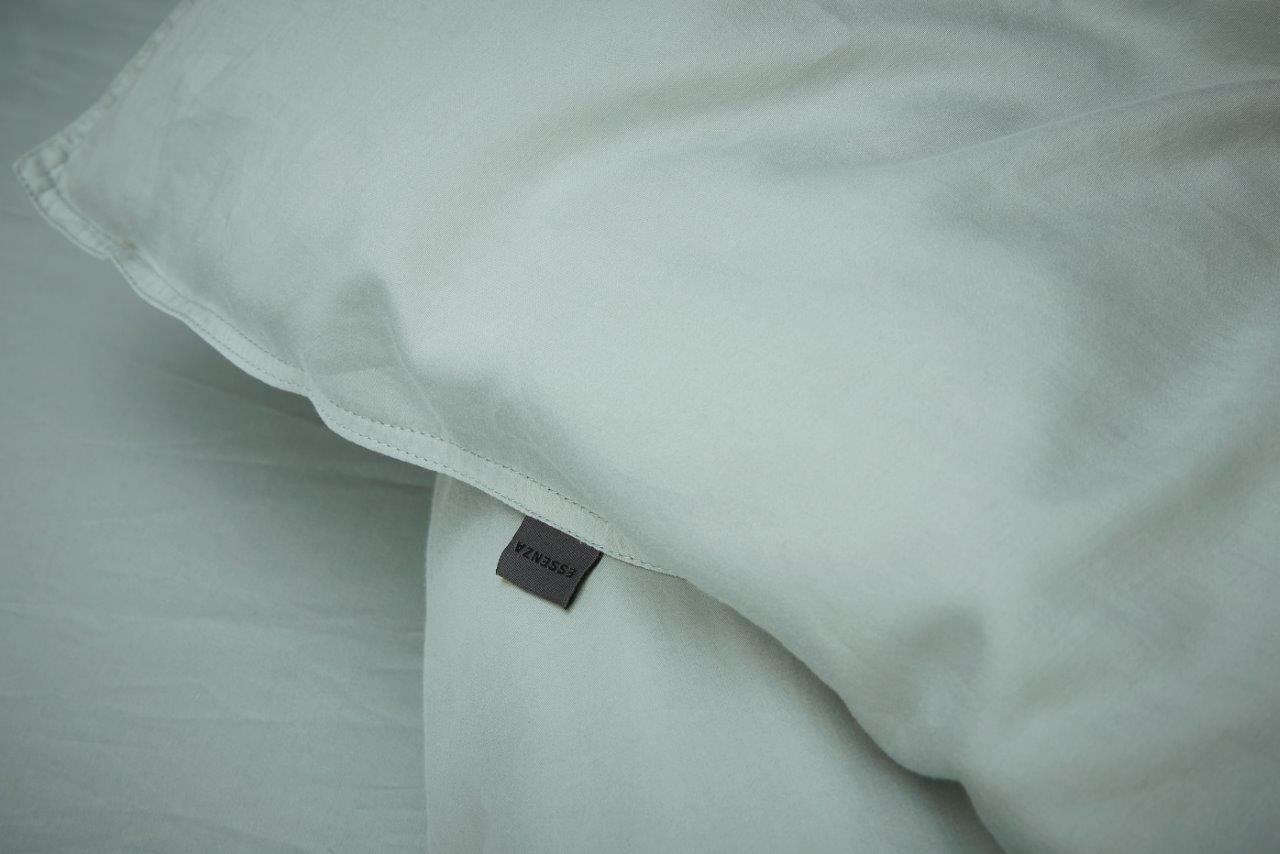 Nahaufnahme einer hellgrauen Bettwäsche mit sichtbarem Etikett, Perspektive von oben.