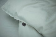 Nahaufnahme einer hellgrauen Bettwäsche mit sichtbarem Etikett, Perspektive von oben.
