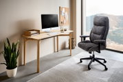 Moderner Homeoffice-Drehstuhl in Grau, seitliche Perspektive, neben einem Schreibtisch mit Computer und Pflanzen, mit Blick auf eine große Fensterfront.