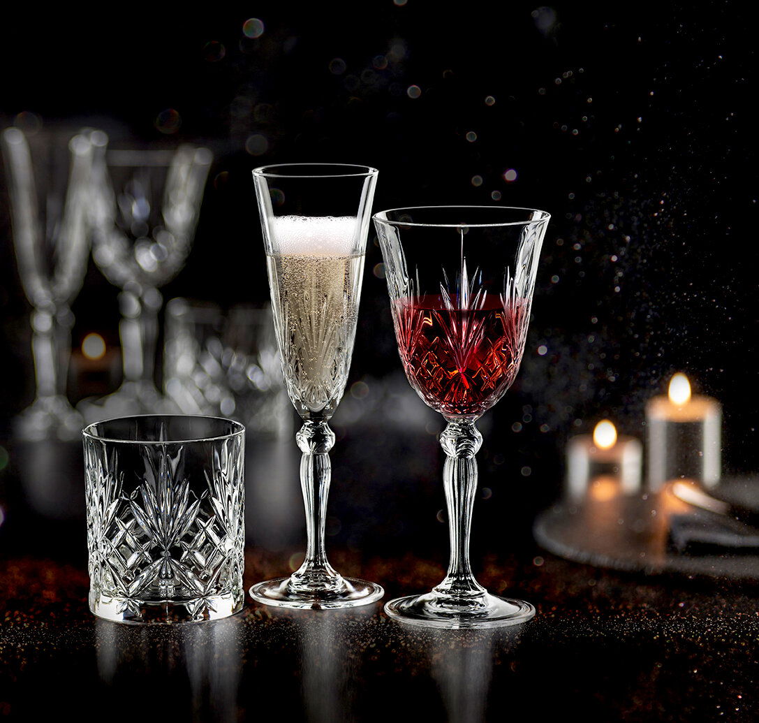 RCR Italia Becherset 18-tlg. MELODIA Drei elegante Kristallgläser, eines mit Sekt, eines mit Rotwein und eines leer, auf einem dunklen, stimmungsvollen Hintergrund mit Kerzenlicht.