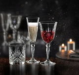 Drei elegante Kristallgläser, eines mit Sekt, eines mit Rotwein und eines leer, auf einem dunklen, stimmungsvollen Hintergrund mit Kerzenlicht.