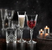 Drei elegante Kristallgläser, eines mit Sekt, eines mit Rotwein und eines leer, auf einem dunklen, stimmungsvollen Hintergrund mit Kerzenlicht.
