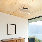 Moderne Deckenleuchte mit drei Glühbirnen, montiert an einer Holzleiste, in einem Raum mit Holzdecke und Panoramafenster. Perspektive von unten.