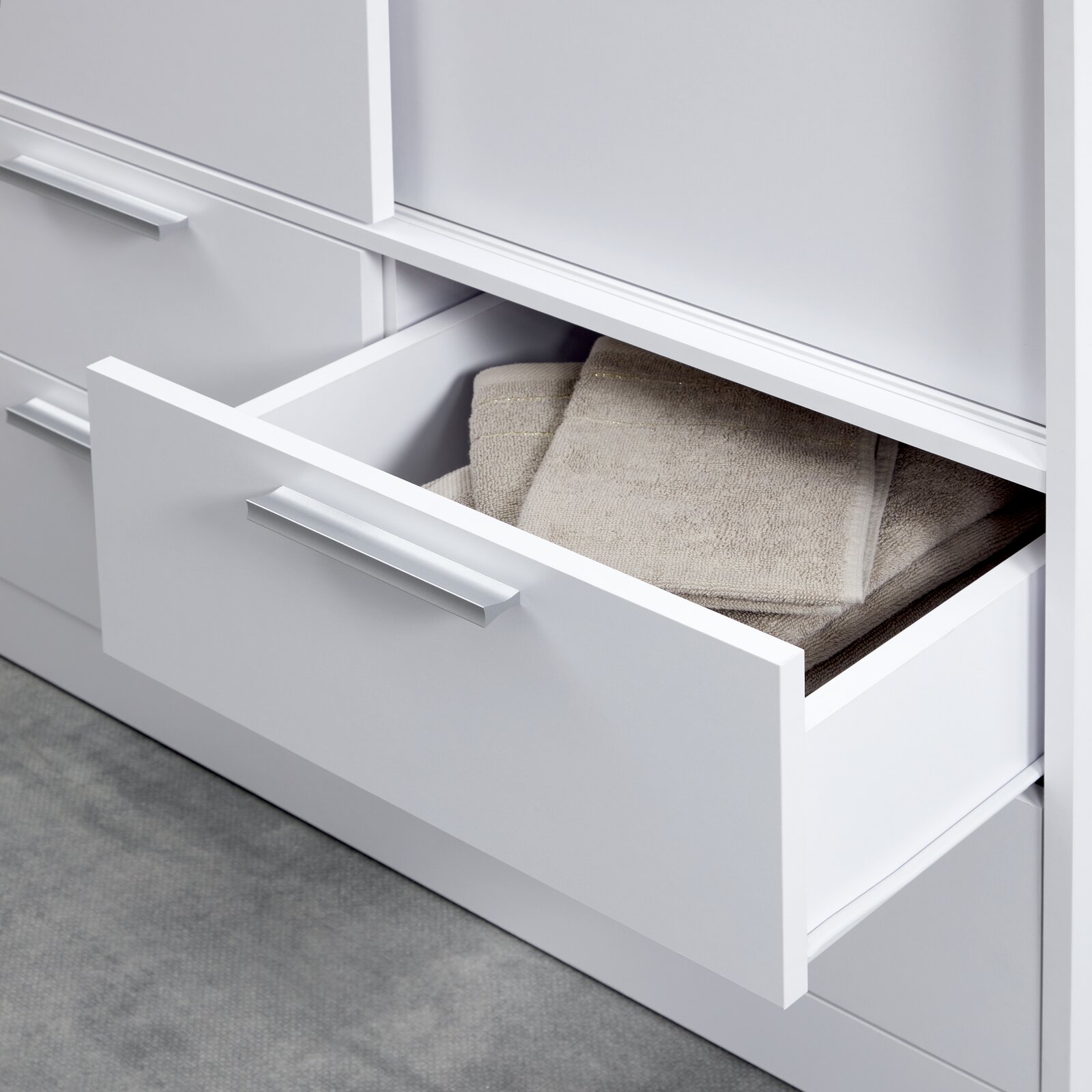 Nahaufnahme eines weißen Schiebetürenschranks mit offener Schublade, gefüllt mit Handtüchern, von der Seite betrachtet.