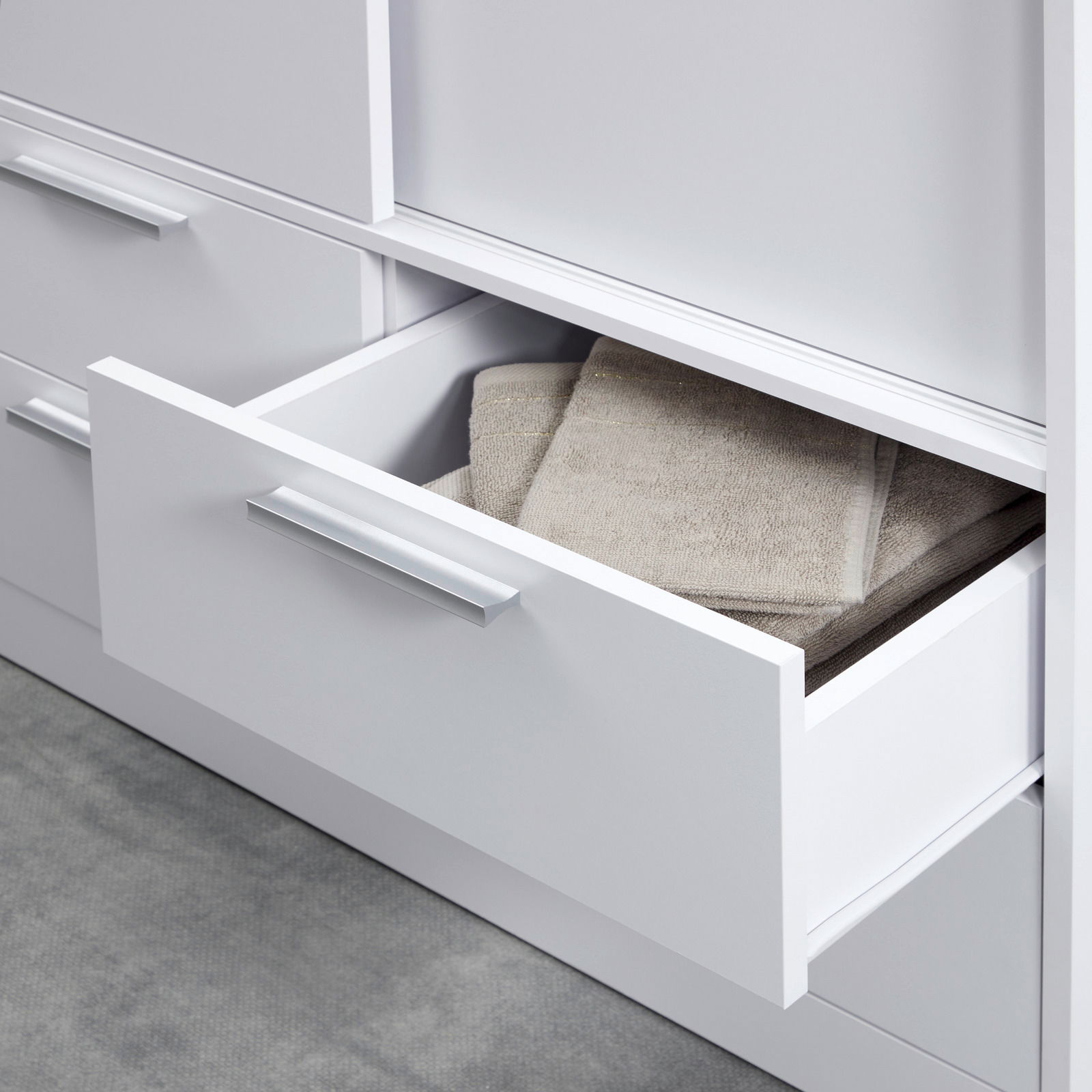 Nahaufnahme eines weißen Schiebetürenschranks mit offener Schublade, gefüllt mit Handtüchern, von der Seite betrachtet.