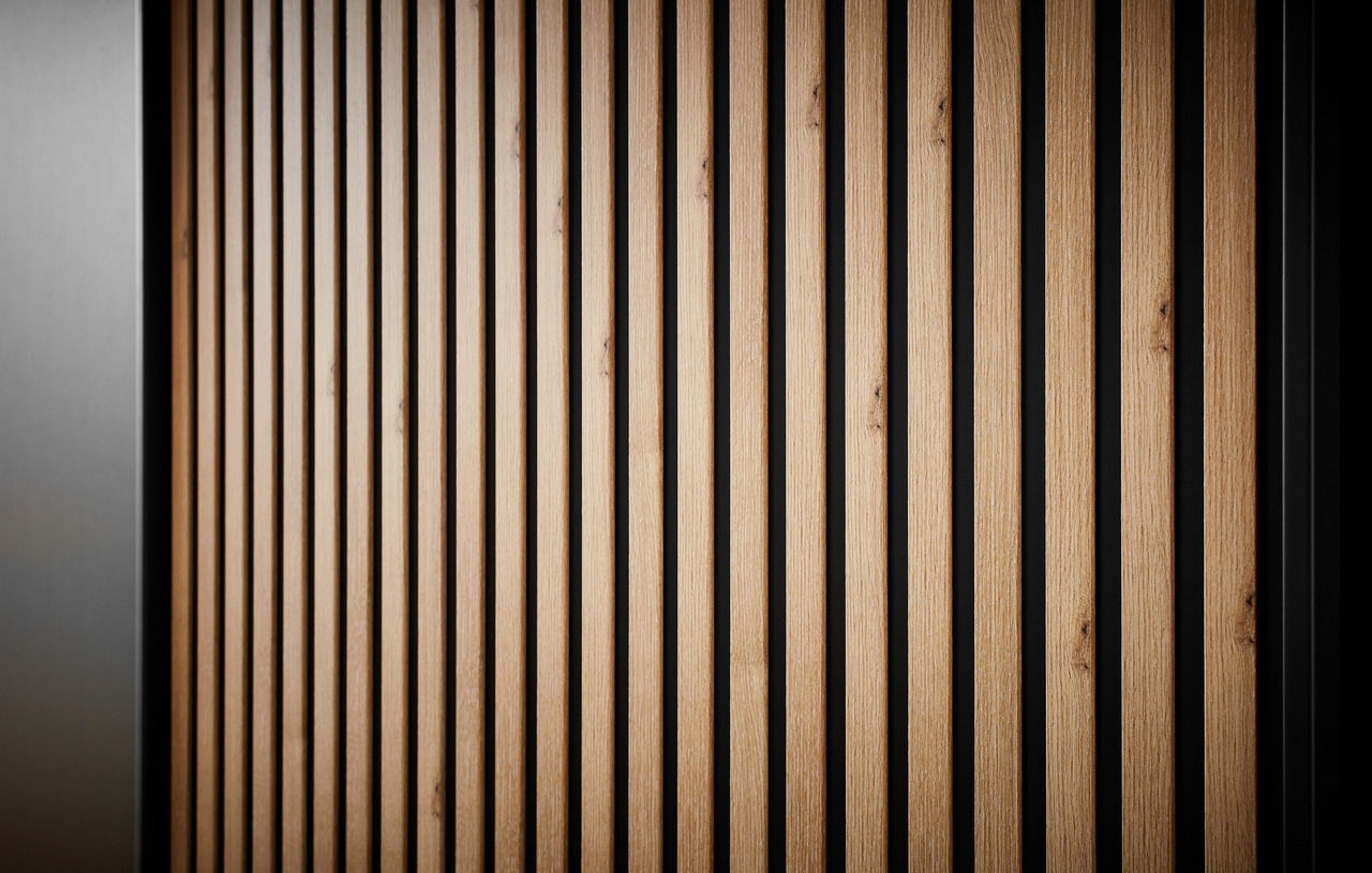 Nahaufnahme eines Schwebetürenschranks mit vertikalen Holzlamellen und schwarzem Hintergrund, seitliche Perspektive