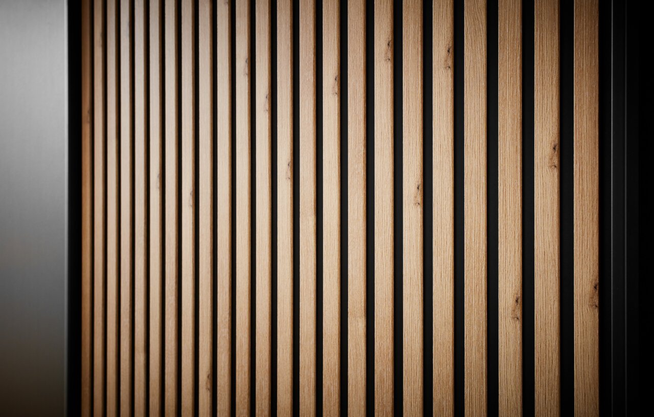 Close-up van een kast met schuifdeuren, verticale houten lamellen en een zwarte achtergrond, gezien vanuit de zijkant