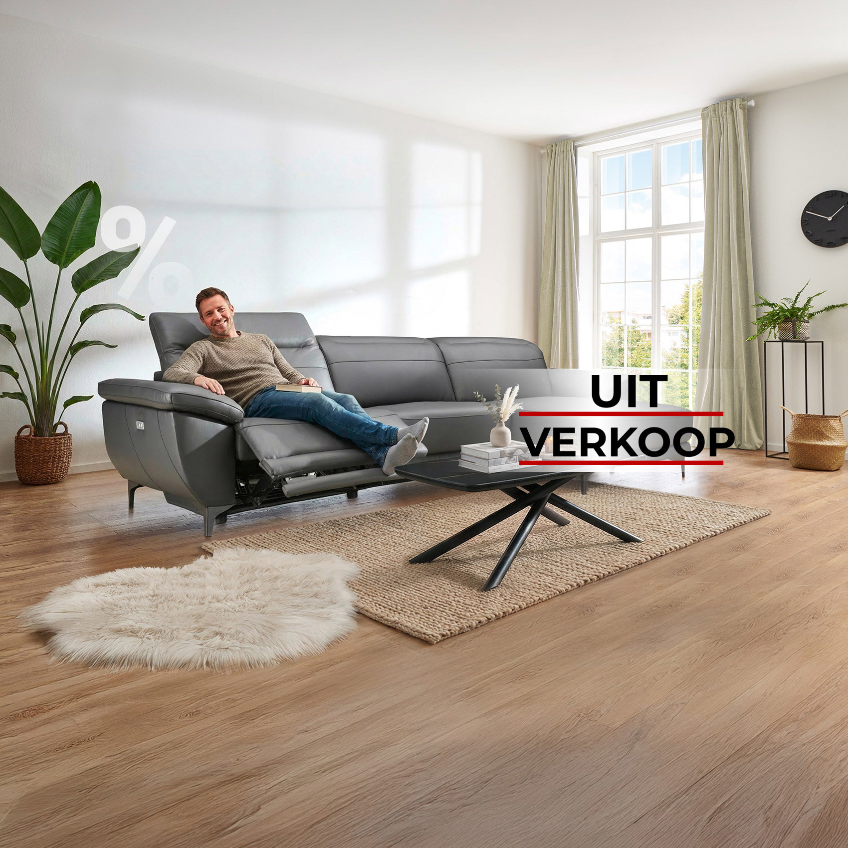 Man ontspant op grijze leren bank in woonkamer, uitverkoop met tot 77% korting.