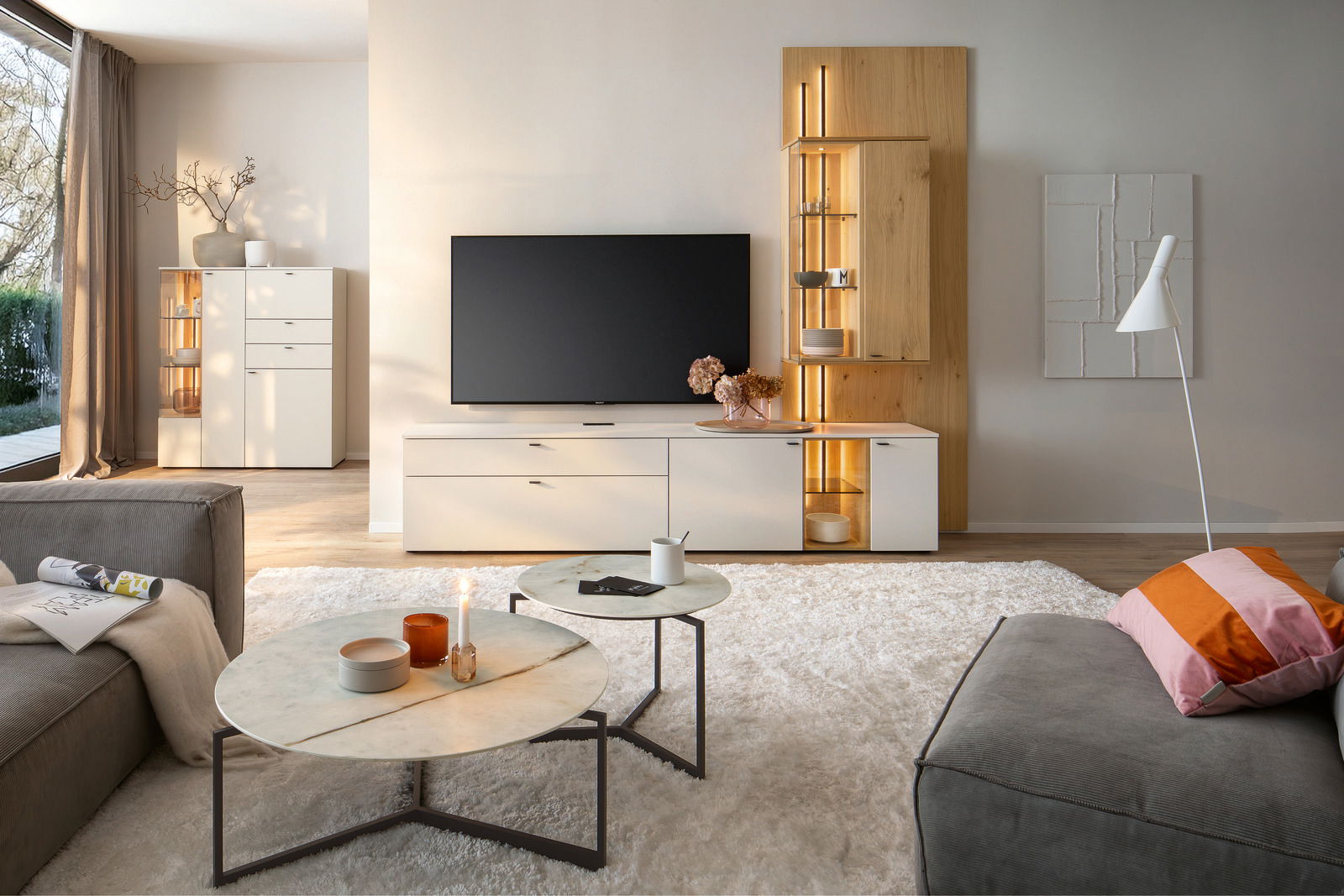 Moderne Wohnzimmer-Wandkombination mit TV, weißen Schränken und Holzakzenten, aus der Perspektive eines gemütlichen Wohnzimmers mit Sofa und Couchtischen.