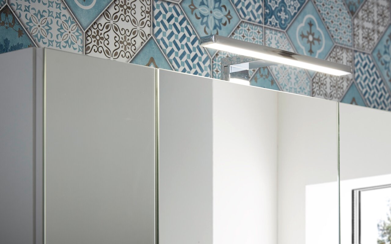 Spiegelschrank mit moderner LED-Beleuchtung, seitliche Perspektive, vor einer Wand mit blau-weißen Fliesen.