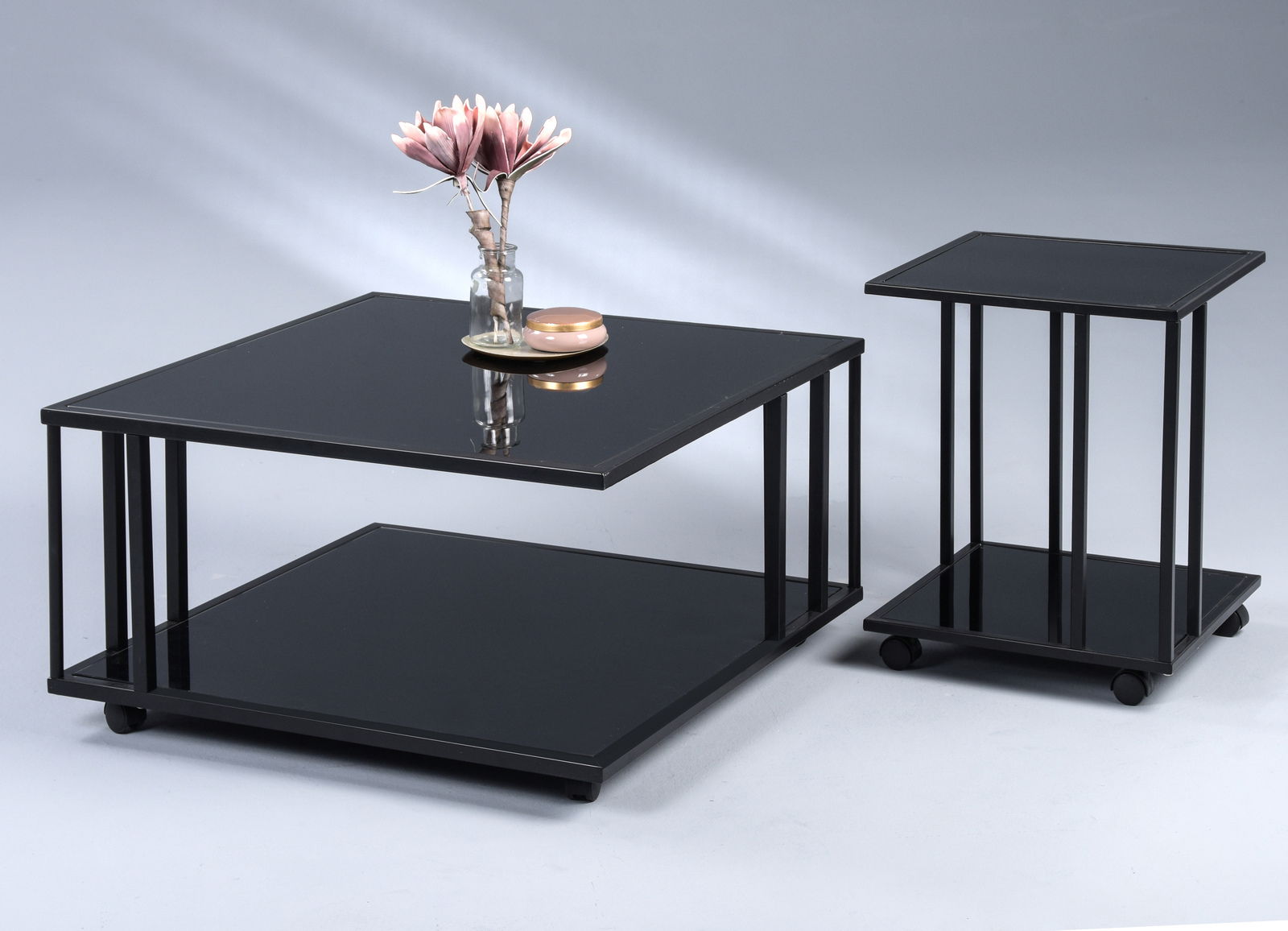 Zwei moderne Tische mit schwarzer Glasoberfläche, ein Beistelltisch und ein Couchtisch, aus seitlicher Perspektive fotografiert.