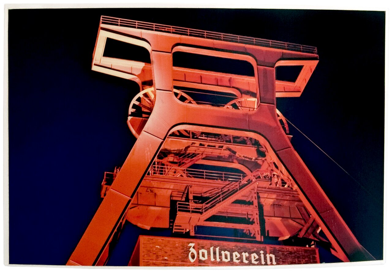 Nachtfoto van de rood verlichte schachttoren van de Zollverein-kolenmijn, genomen vanuit een licht opwaarts gericht perspectief.