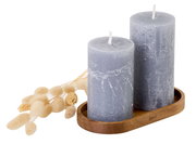 Zwei graue Kerzen auf einem Untersetzer aus Akazienholz, seitliche Perspektive, mit dekorativen Trockenblumen.