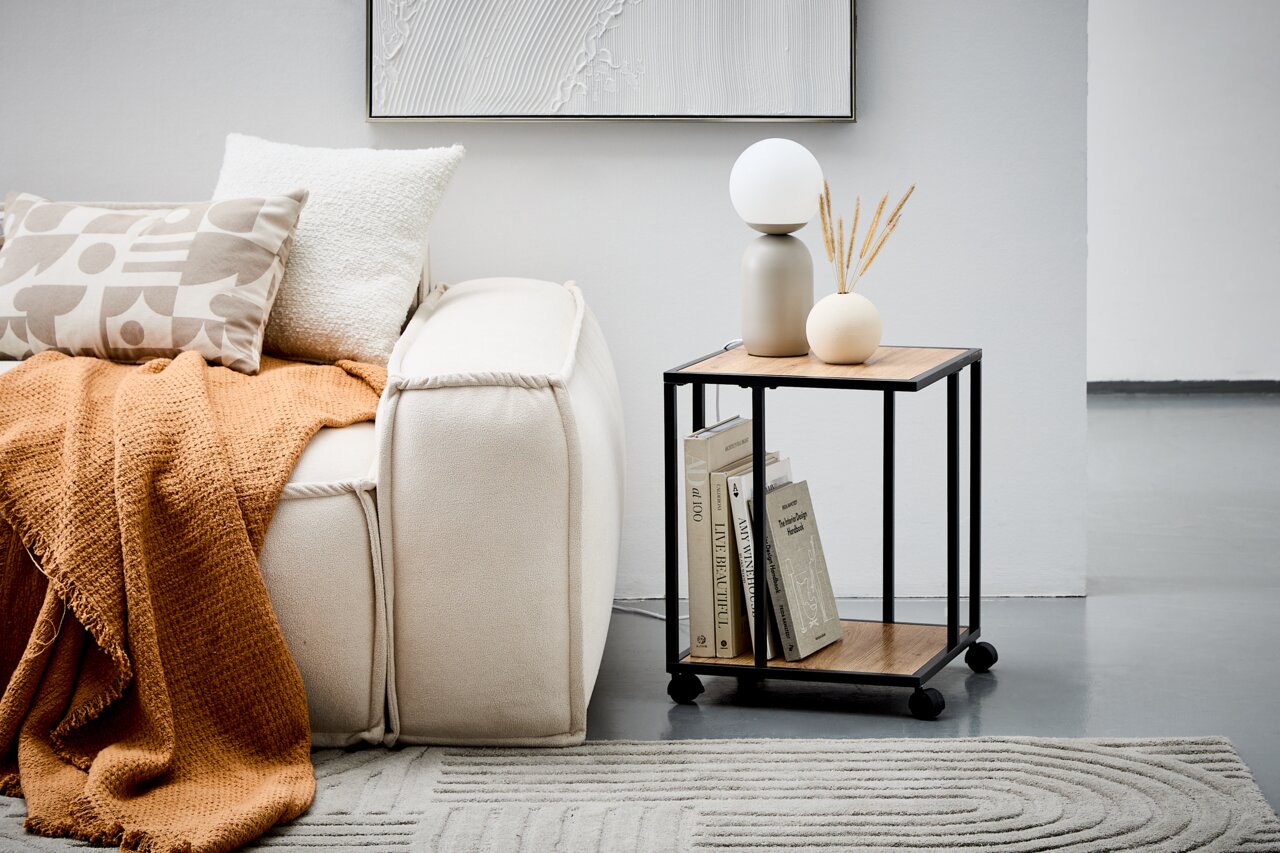 Moderner Beistelltisch mit schwarzem Metallrahmen und Holzplatten, dekoriert mit Büchern, einer Lampe und einer Vase, seitliche Perspektive.