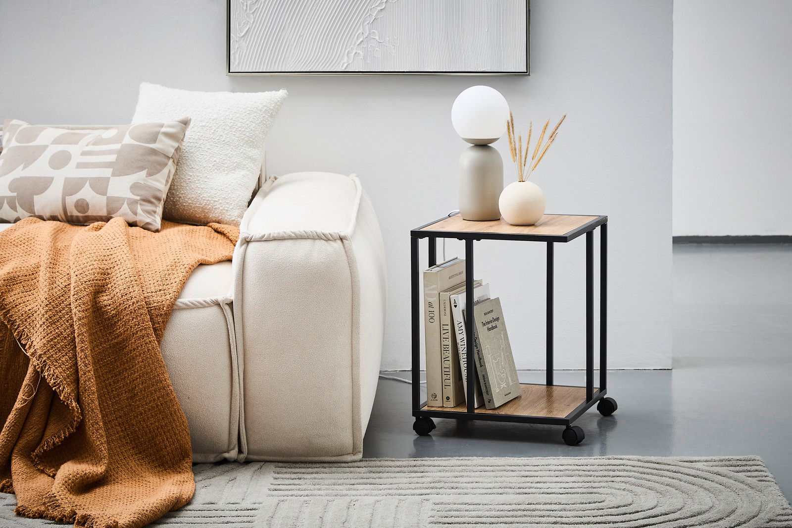 Moderner Beistelltisch mit schwarzem Metallrahmen und Holzplatten, dekoriert mit Büchern, einer Lampe und einer Vase, seitliche Perspektive.