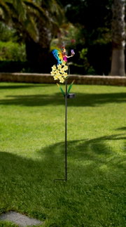 Kleurrijke zonne-lamp in de vorm van een bloem met een vlinder, rechtop in de tuin, zijaanzicht.