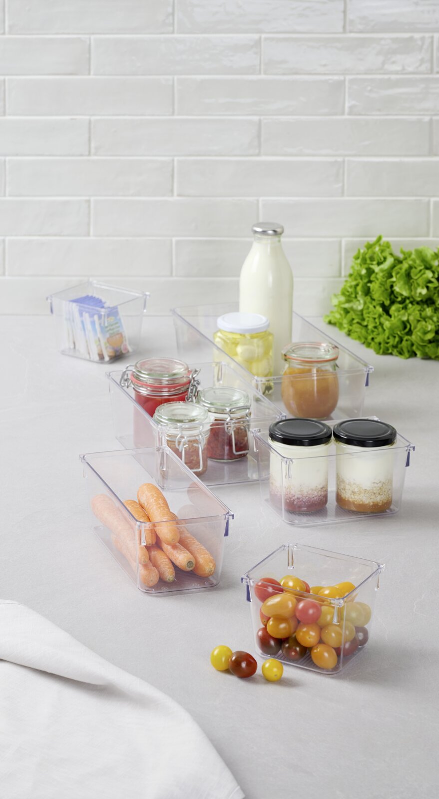 Homeware Organizer, 10-delig Doorzichtige opbergbakjes in verschillende maten, gevuld met etenswaren zoals wortelen, tomaten en yoghurt, op een keukenblad. Perspectief van schuin bovenaf.