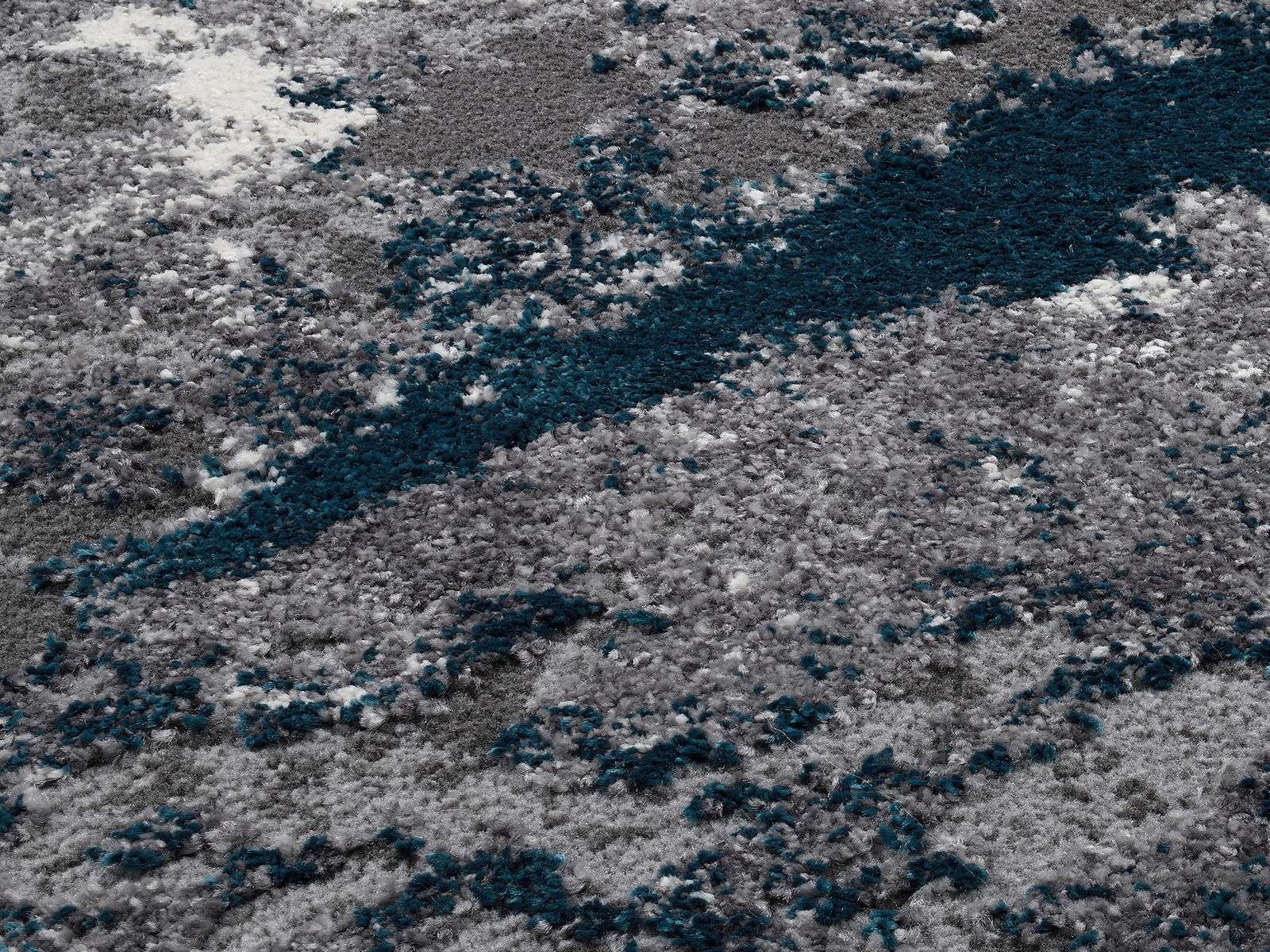 Nahaufnahme eines Designer-Teppichs mit grauen, weißen und blauen Farbtönen in einer strukturierten, flauschigen Oberfläche.
