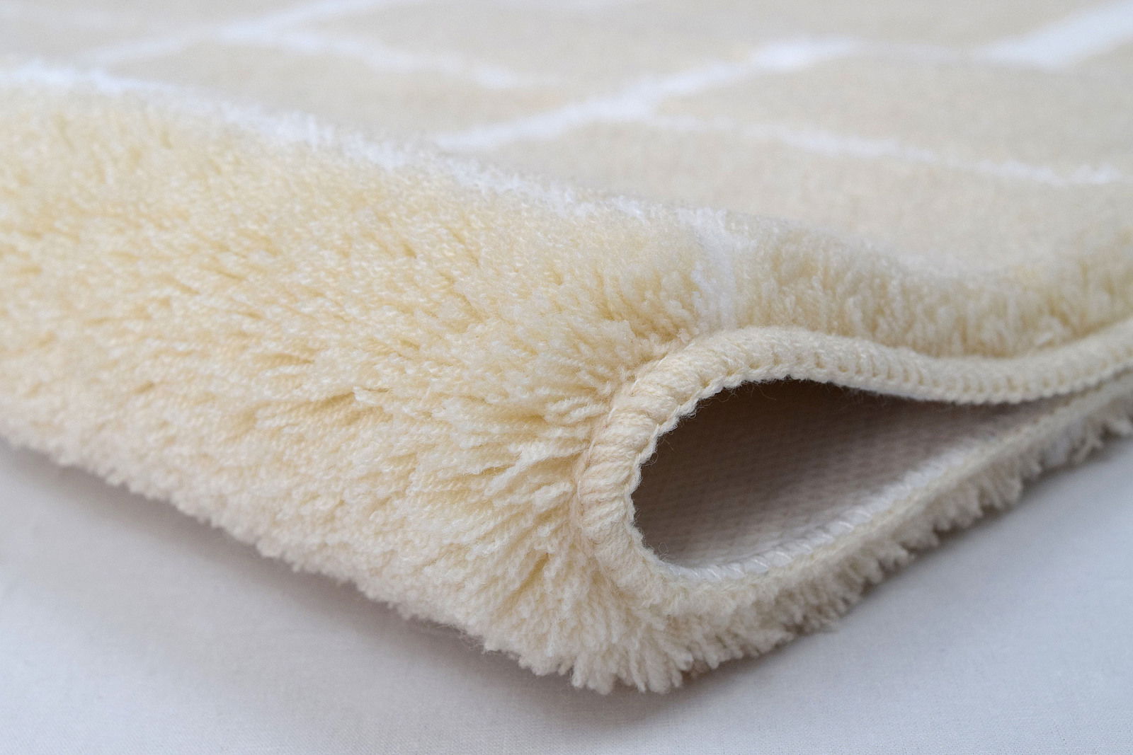 Nahaufnahme eines cremefarbenen, flauschigen Badteppichs in gerollter Perspektive.