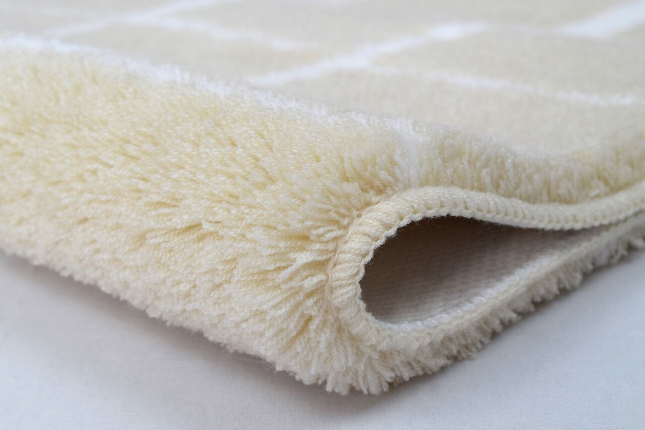 Kleine Wolke Badteppich CARAT Nahaufnahme eines cremefarbenen, flauschigen Badteppichs in gerollter Perspektive.