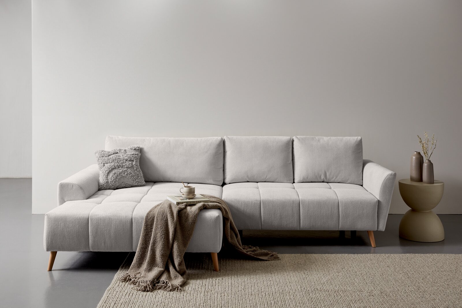 Z2 Ecksofa ZELDA Modernes hellgraues Ecksofa mit Recamiere links, gesteppten Sitzflächen und Holzfüßen in minimalistischer Wohnszene, Frontansicht auf Augenhöhe.