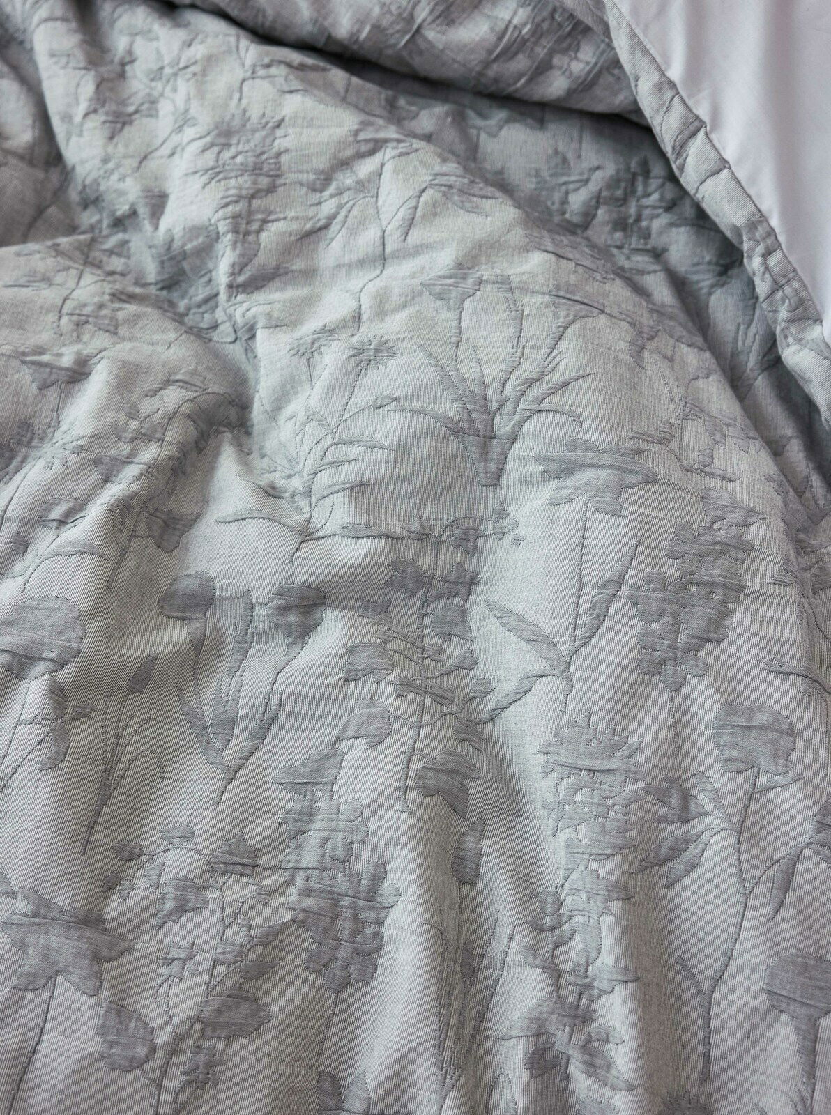 Nahaufnahme einer grauen Bettwäsche mit floralem Muster, aus der Vogelperspektive fotografiert.