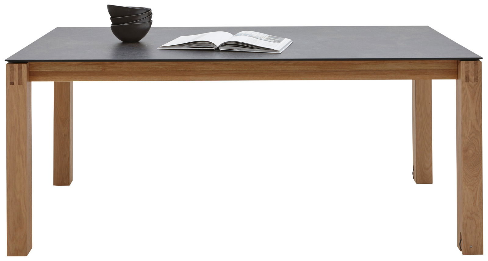 Moderner Esstisch mit dunkler Tischplatte und hellen Holzbeinen, frontal fotografiert. Auf dem Tisch liegen Schalen und ein geöffnetes Buch.