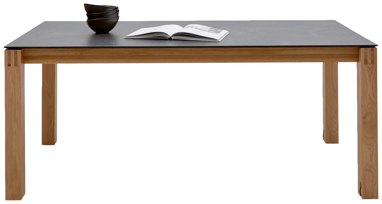 Moderner Esstisch mit dunkler Tischplatte und hellen Holzbeinen, frontal fotografiert. Auf dem Tisch liegen Schalen und ein geöffnetes Buch.