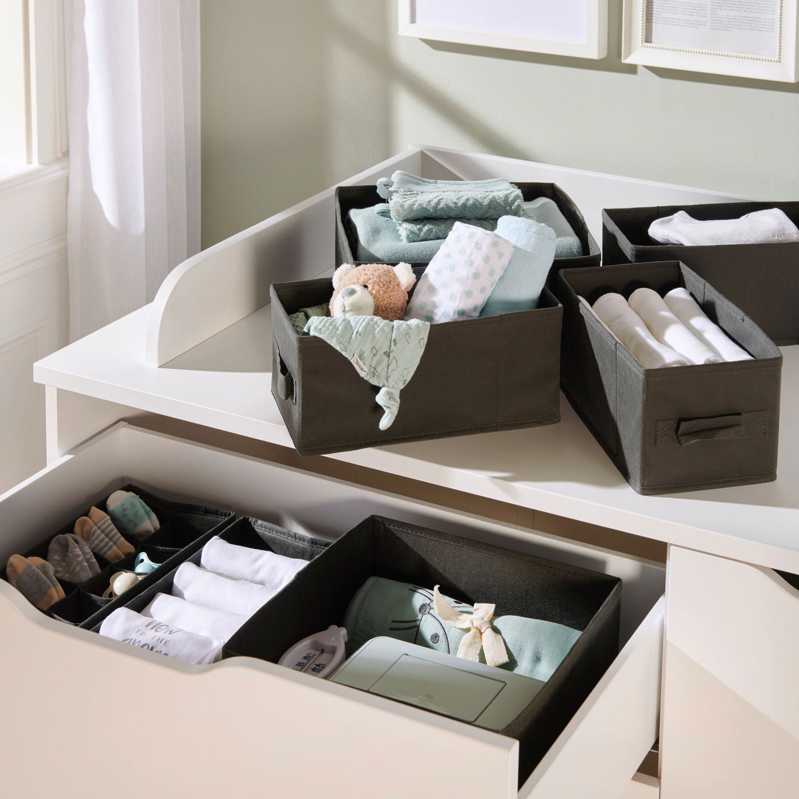 Aufbewahrungsboxen-Set in einer Schublade und auf einer Kommode, gefüllt mit Babyartikeln, aus der Vogelperspektive fotografiert.