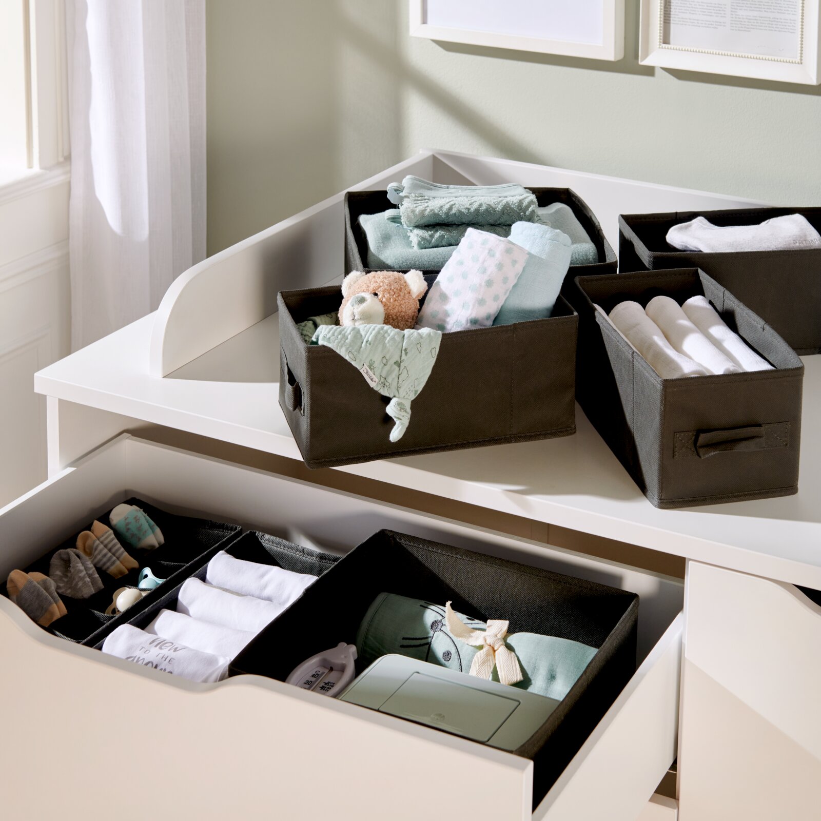 Set opbergdozen in een lade en op een commode, gevuld met babyspullen, gefotografeerd vanuit vogelperspectief.
