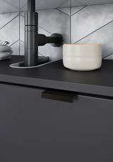 Nahaufnahme eines modernen Waschbeckenunterschranks in dunklem Design mit schwarzem Wasserhahn und cremefarbener Schale, seitliche Perspektive.