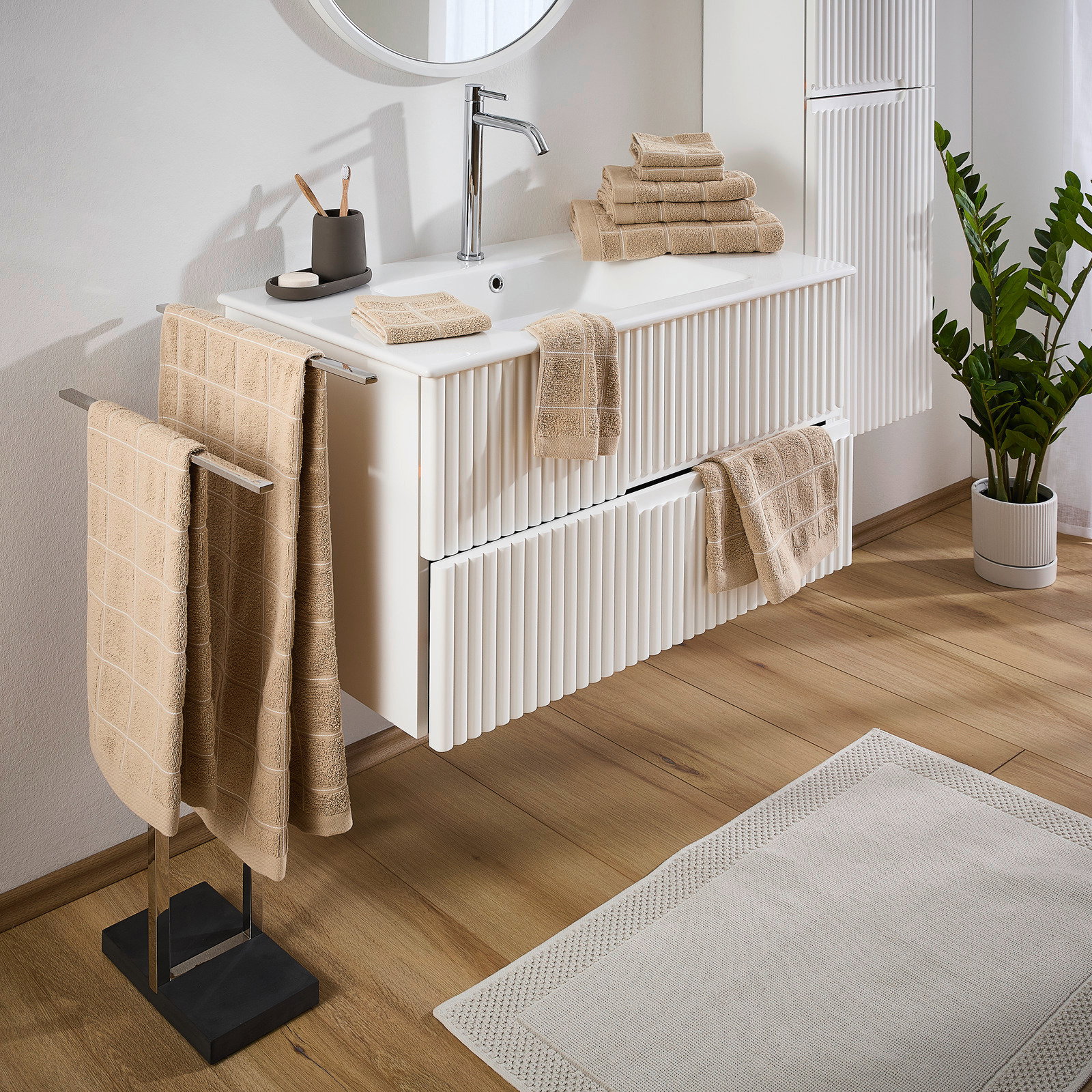 Beige Frottierset in einem modernen Badezimmer, mit Handtüchern auf einem Handtuchhalter und einem Waschtisch, seitliche Perspektive
