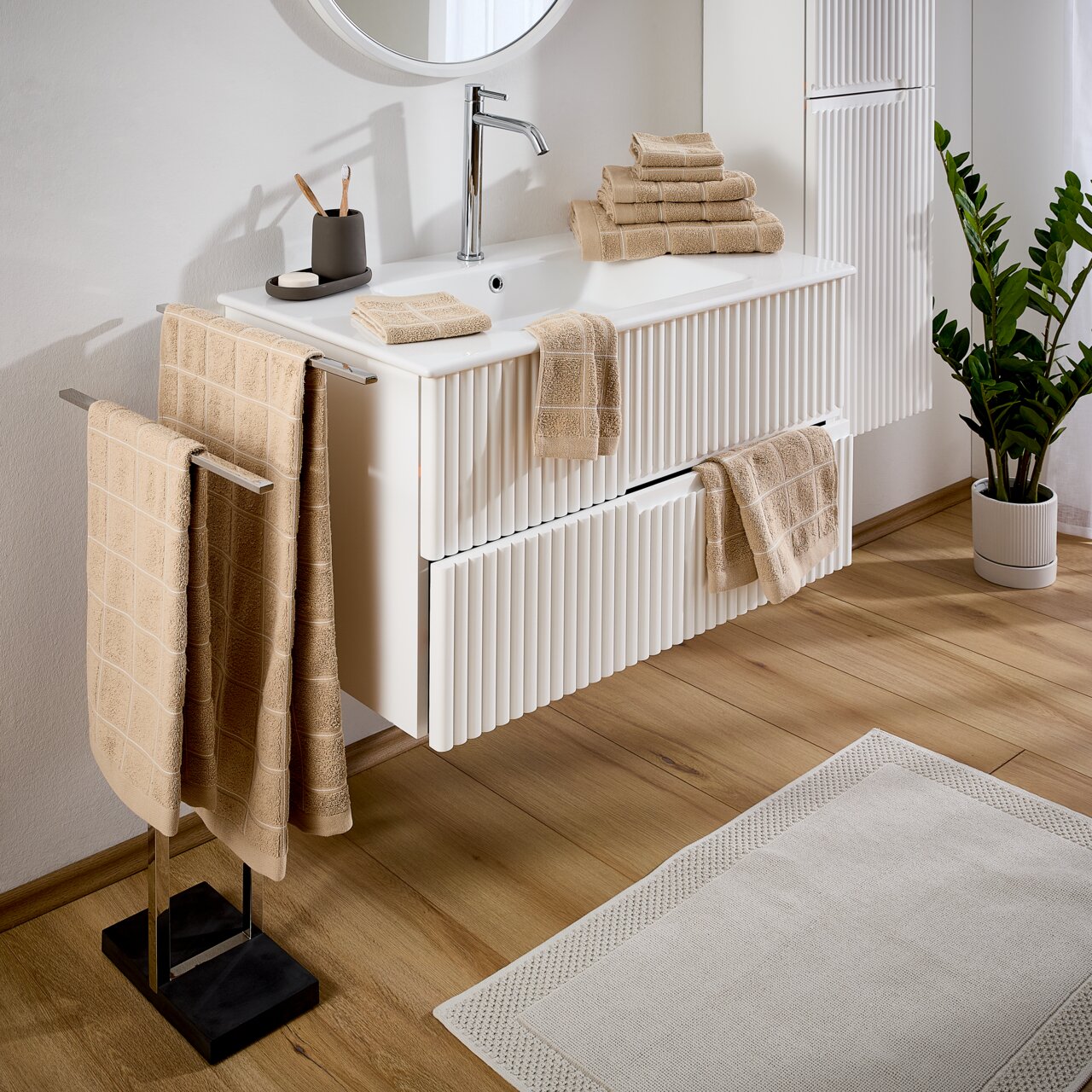 Beige badstofset in een moderne badkamer, met handdoeken op een handdoekrek en een wastafel, zijaanzicht