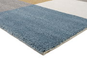 Nahaufnahme eines Uni-Teppichs mit verschiedenen Farbblöcken in Blau, Grau, Beige und Weiß, aus seitlicher Perspektive fotografiert.