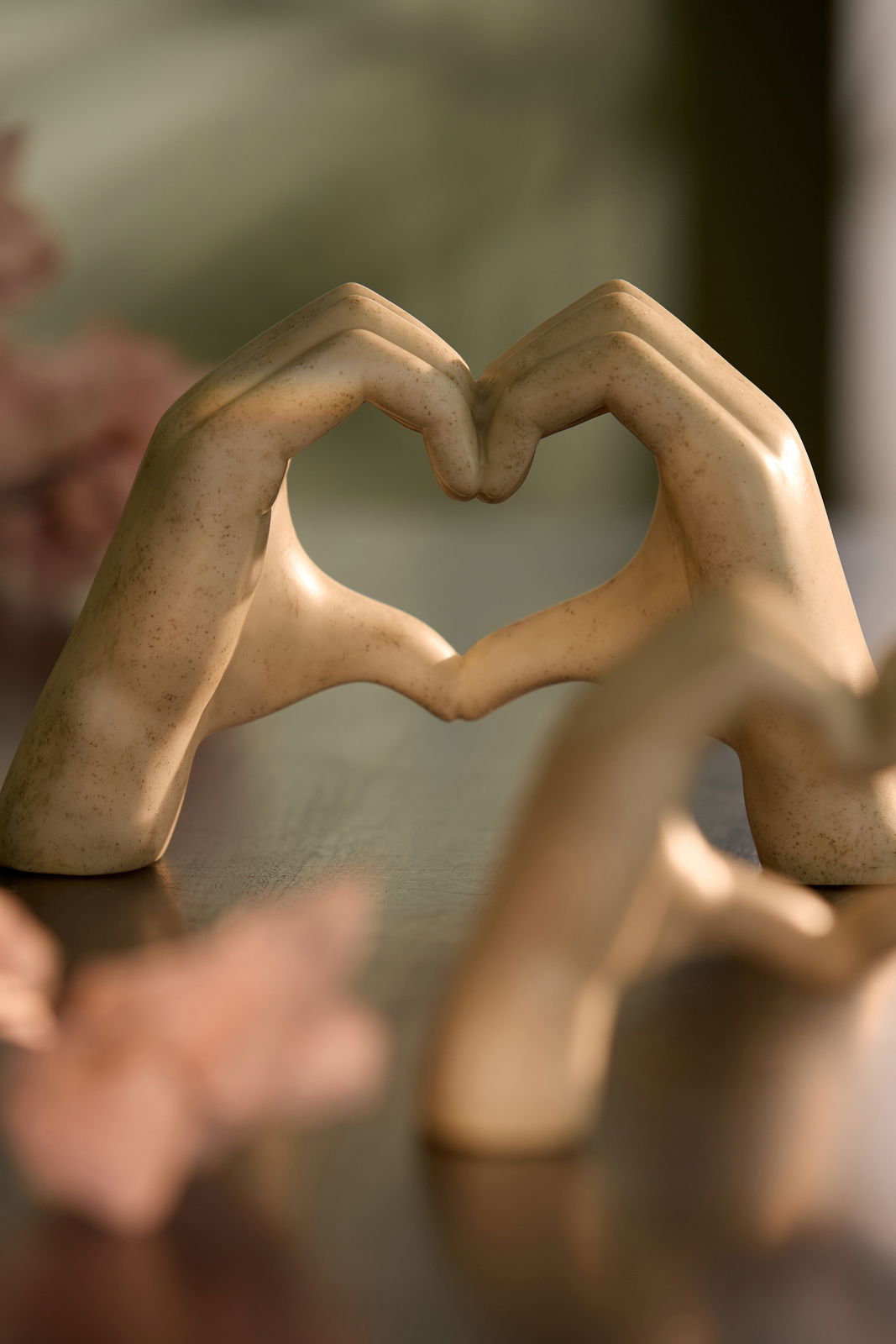 Zwei Hände aus Keramik formen ein Herz, auf einem Tisch stehend, mit unscharfem Hintergrund. Perspektive: seitlich.