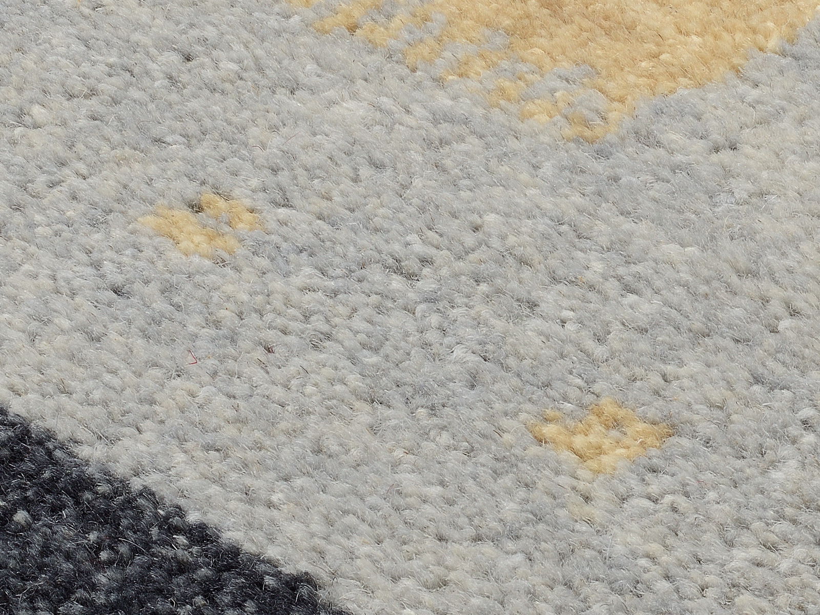 Nahaufnahme eines Wollteppichs mit grauen, schwarzen und beigen Mustern, von oben betrachtet.