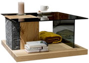 Moderner Couchtisch mit Glasplatte, Holz- und Steinelementen, dekoriert mit einer Kerze, einer Tasse und Büchern, aus seitlicher Perspektive.