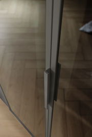 Nahaufnahme eines Griffs an einer Glastür eines sechstürigen Drehtürenschranks, aus seitlicher Perspektive fotografiert.