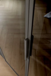 Close-up van een handgreep op een glazen deur van een kast met zes draaideuren, gefotografeerd vanuit een zijaanzicht.
