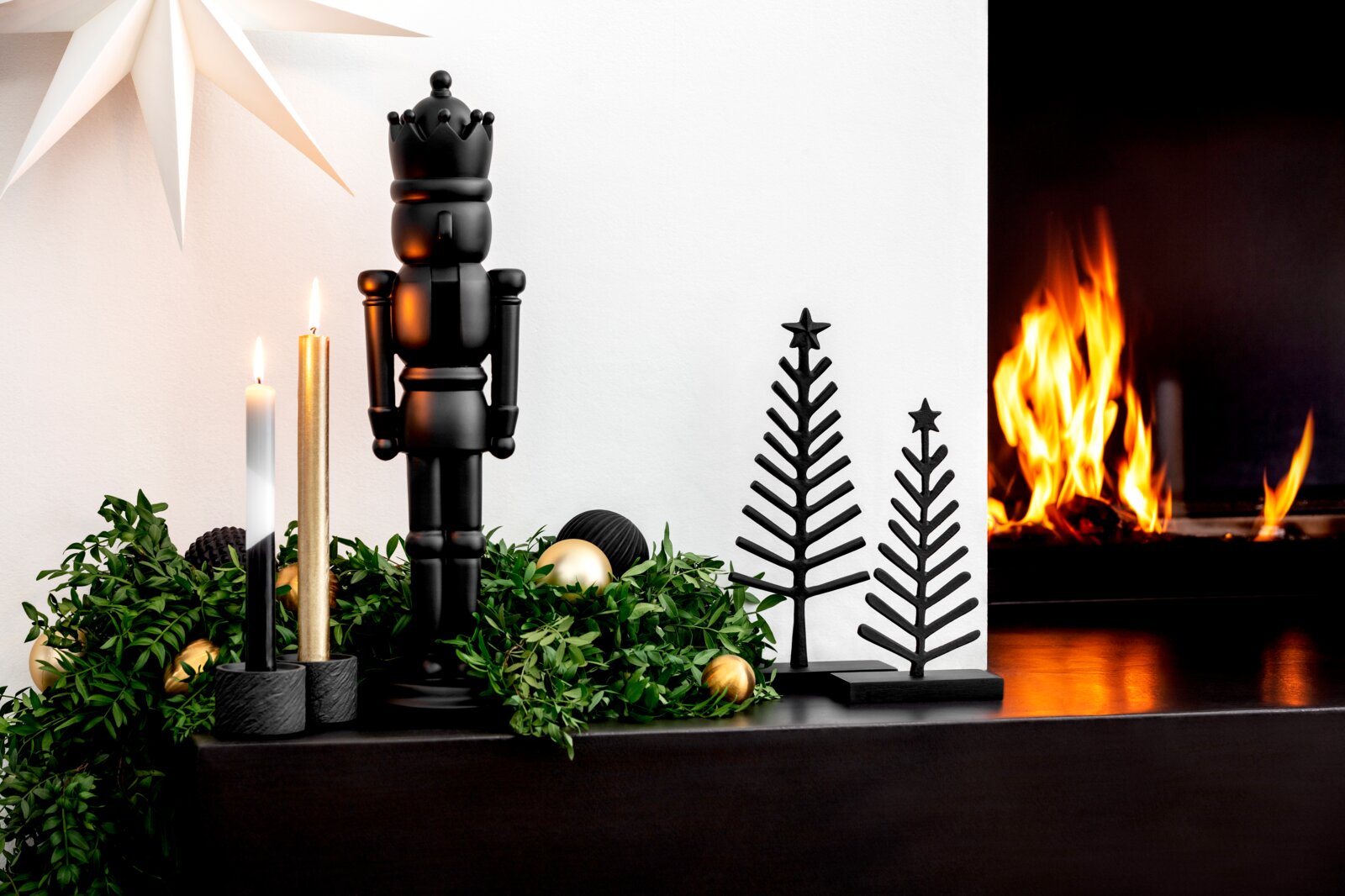 Villeroy & Boch Baum Festliche Weihnachtsdekoration aus schwarzem Nussknacker, zwei stilisierten Tannenbäumen und Kerzen, frontal vor einem brennenden Kamin arrangiert
