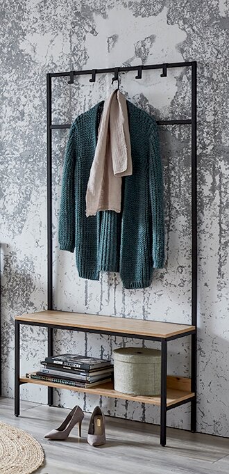 Schwarze Metall-Garderobe mit Holzbank und Ablage, darauf ein grüner Strickcardigan und beiger Schal, Schuhe und Bücher darunter; frontale Perspektive.