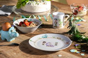 Kindergeschirrset mit Dinosaurier-Motiven, bestehend aus einem Teller, einer Schale und einer Tasse, auf einem Holztisch arrangiert. Perspektive von oben.