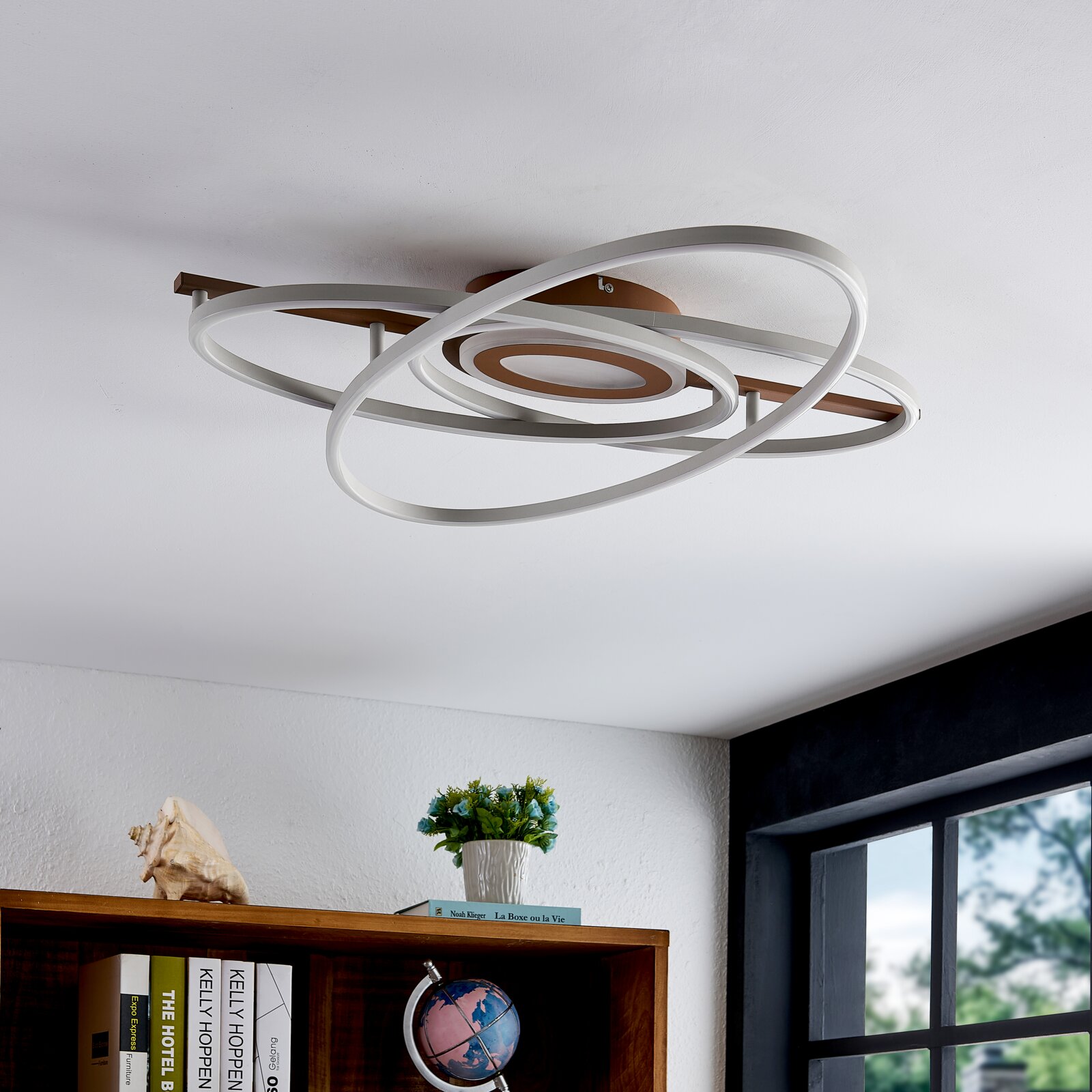 Moderne LED plafondlamp met overlappende ringen in wit en bronskleurig metaal, gezien schuin van onderen tegen een witte plafond in een interieur.