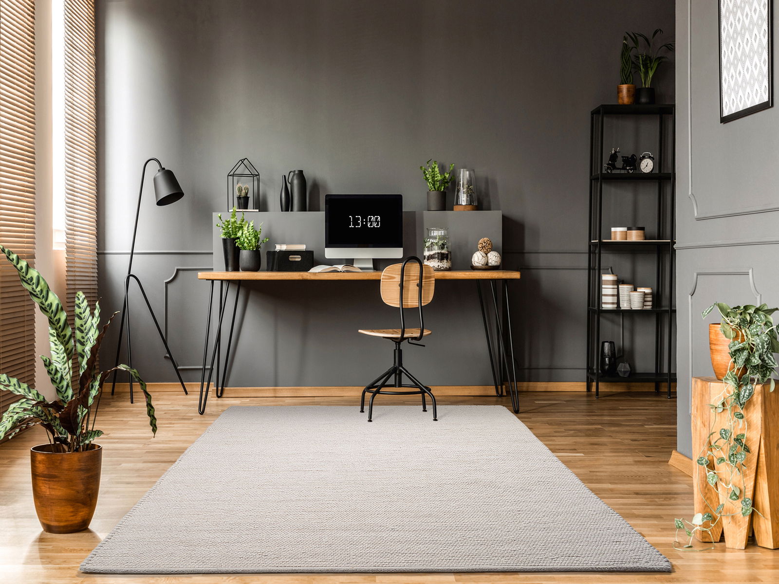 OCI Handweb Teppich FAVORIT Moderner Arbeitsbereich mit einem hellgrauen Handweb Teppich im Vordergrund, der auf einem Holzboden liegt. Der Raum ist stilvoll eingerichtet mit einem Schreibtisch, Pflanzen und dekorativen Elementen. Perspektive von vorne auf den Teppich gerichtet.